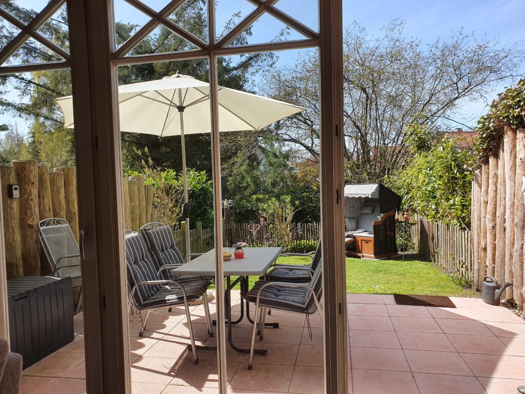 Eingezäunter Garten des Ferienhauses mit Terrasse, Strandkorb, Sonnenschirm und Terrassenmöbeln.