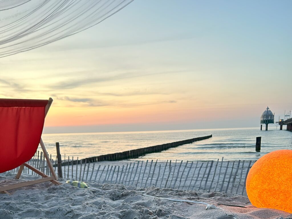 Strand mit rotem Liegestuhl und Seebrücke von Zingst bei Sonnenuntergang