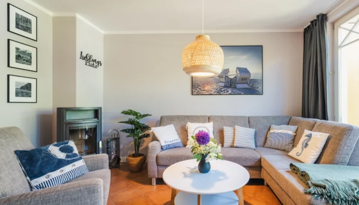 Eckcouch mit Kamin im Wohnbereich des Ferienhaus Herzmuschel in Zingst. An der Wand hängt ein großes Bild mit Strandkorb.
