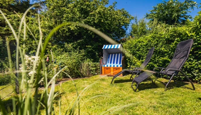 Garten des Ferienhaus Herzmuschel in Zingst. Man sieht eine grüne Wiese mit zwei Sonnenliegen und einem blau weiß gestreiften Strandkorb.