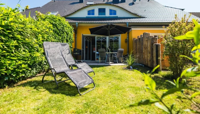 Rückseite des Ferienhaus Herzmuschel in Zingst. Man sieht den vollständig eingezäunten Garten, zwei Sonnenliegen und die Terrasse.