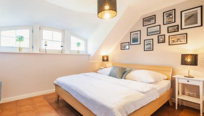 Großzügiges Schlafzimmer im Ferienhaus Herzmuschel in Zingst mit großem Doppelbett. Über dem Bett hängen dekorative Bilder vom Strand in Zingst.