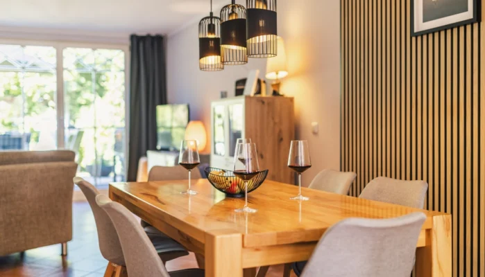 Essbereich für 6 Personen im Ferienhaus Herzmuschel in Zingst. Auf dem Holztisch stehen Weingläser. Die Wand ist mit modernen Akustikpaneelen verkleidet.