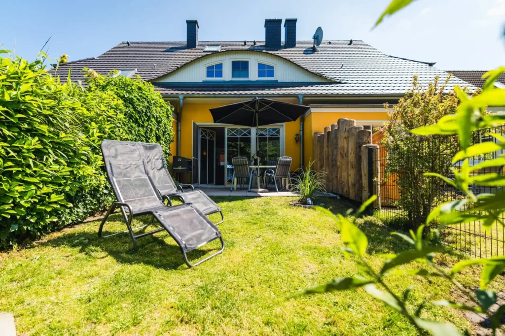 Rückseite der Zingst Ferienwohnung privat. Man sieht den vollständig eingezäunten Garten, zwei Sonnenliegen und die Terrasse.